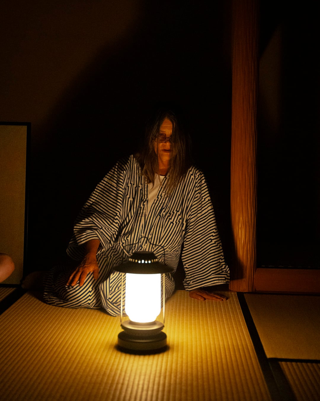 Pojke sitter vid lampa på golv. Foto.