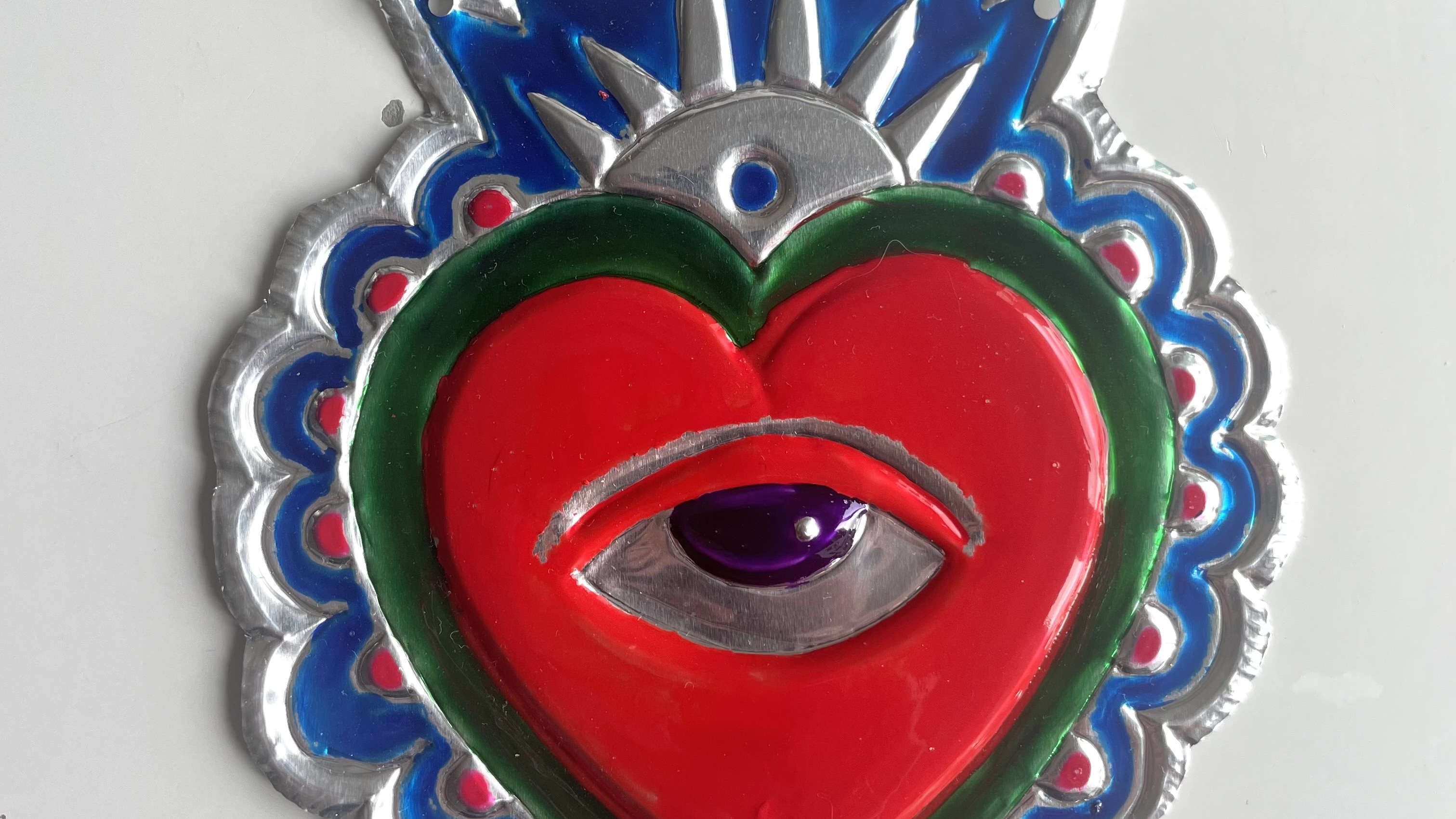 Amulett i mjuk metall i form av ett hjärta med ett öga i mitten